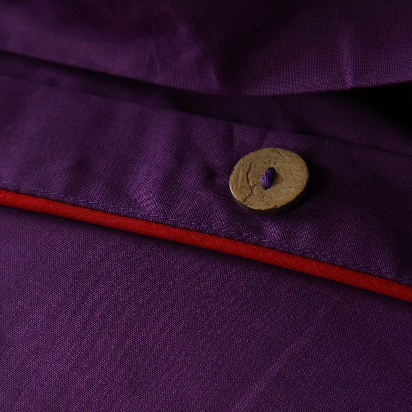 Close-up of a natural coconut button on a BUTTIA purple duvet cover with red piping.