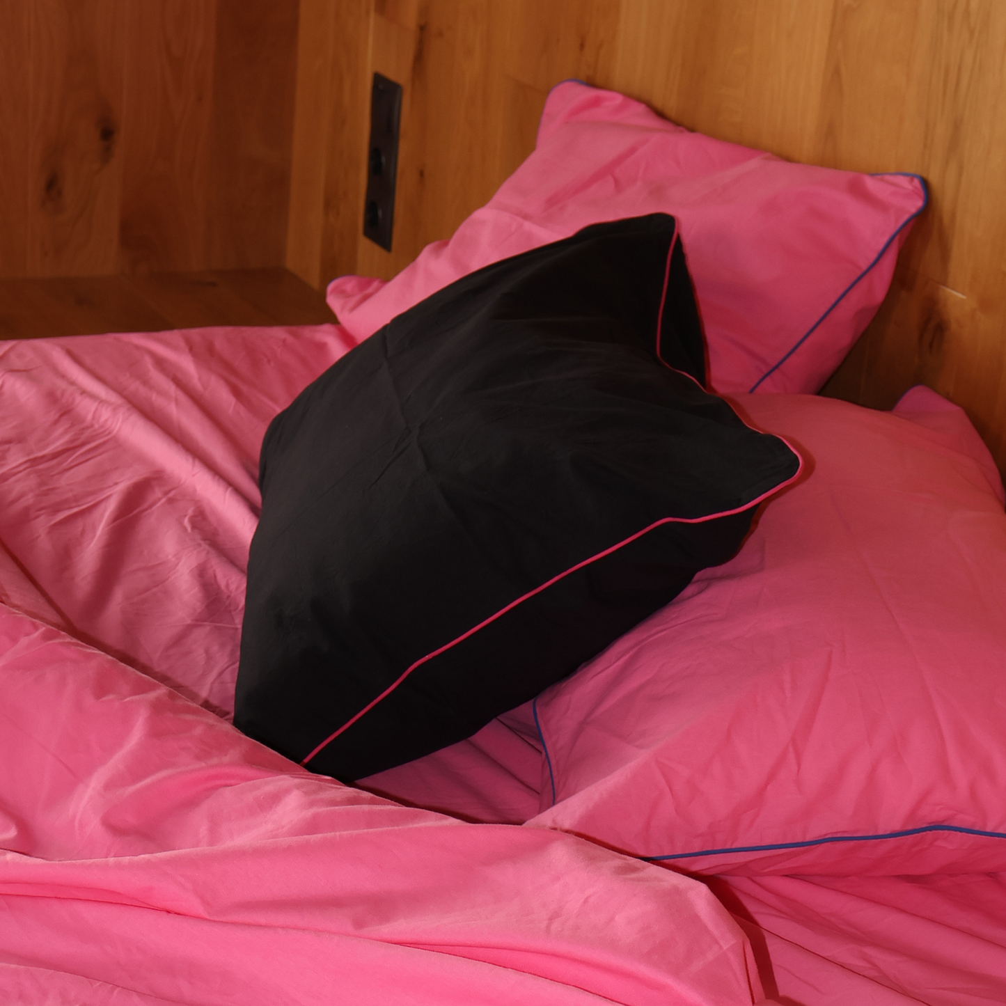 Pink bedding with black pillow on a wooden bed frame