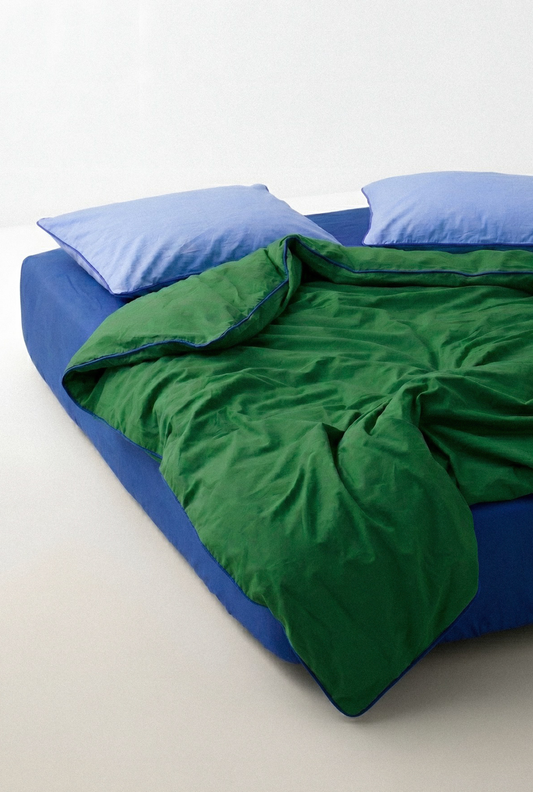 Blue bed with green comforter and blue pillows on a white background