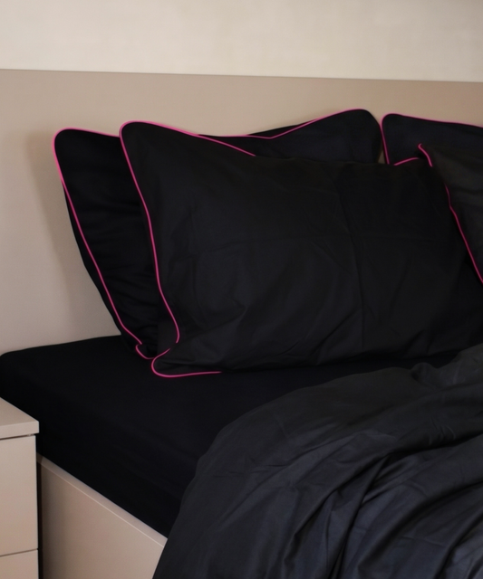 Black pillows with pink piping on a bed against a beige wall.