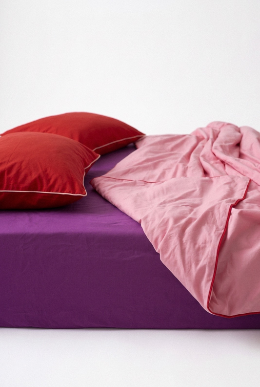 Purple bed with pink blanket and red pillows on a white background