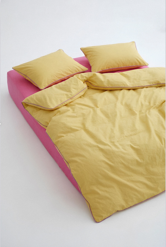 Yellow comforter and pillows on a pink bed frame against a white background