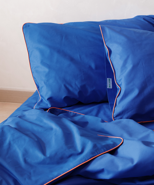 Blue bedding set BUTTIA with orange piping on a bed against a white wall.
