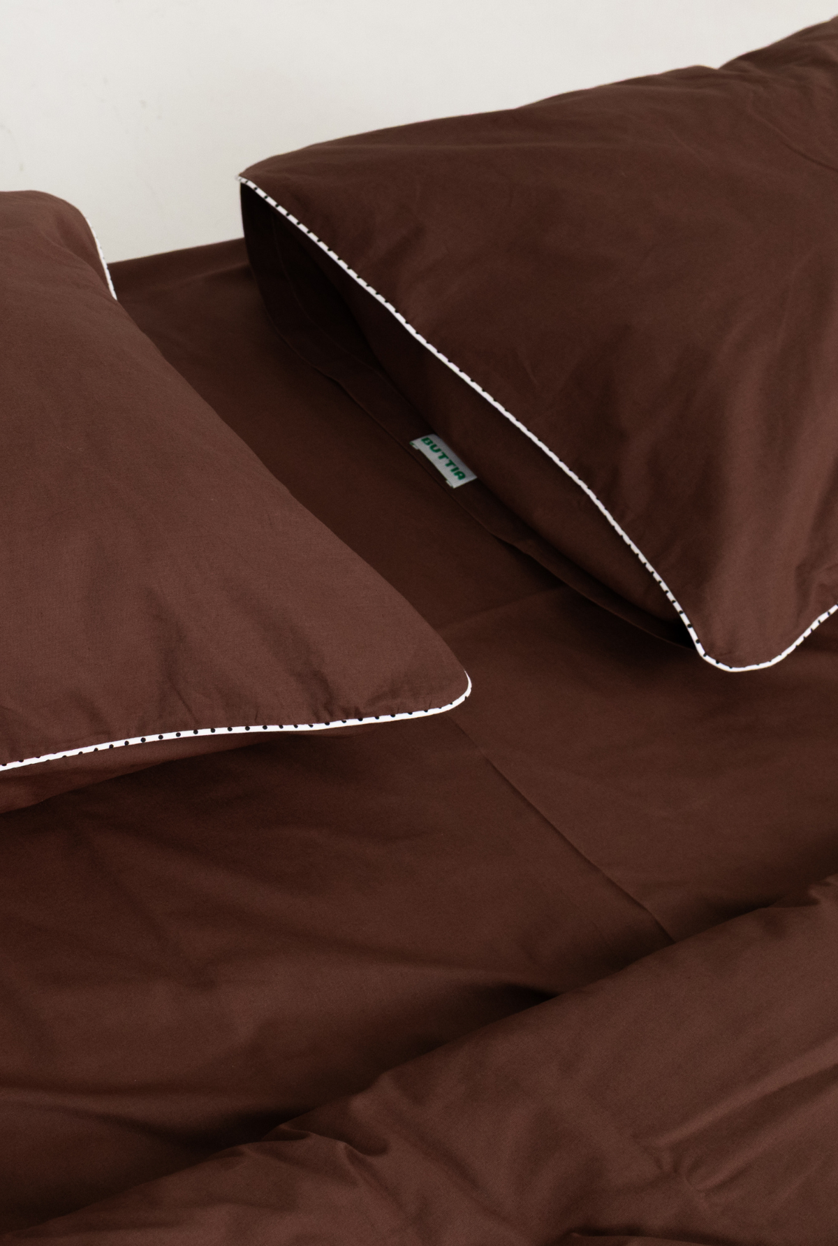 Brown bedding set BUTTIA with matching pillowcases and duvet cover, featuring delicate white contrast stitching along the edges.
