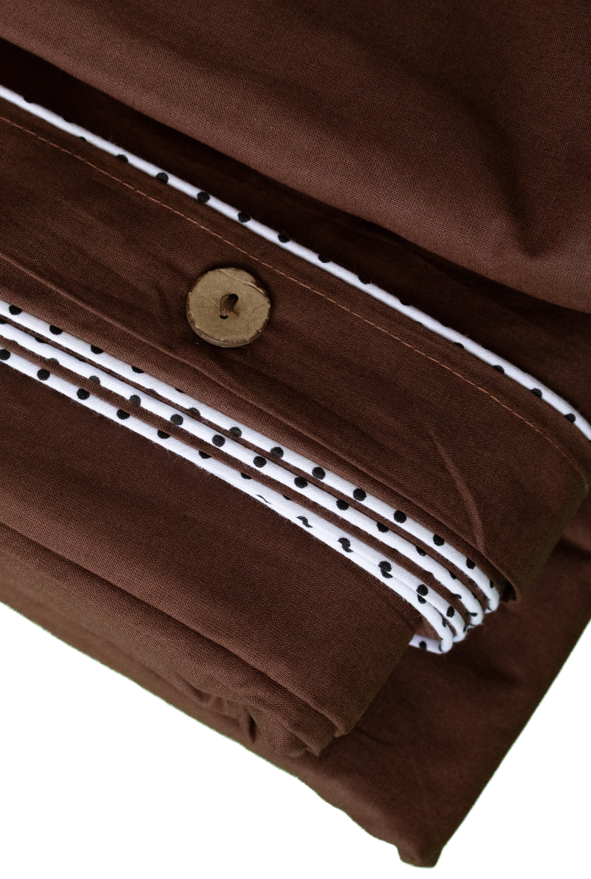 Close-up of folded brown fabric with a white stripe bordered by small black dots and a round brown button closure, shown on a white background.