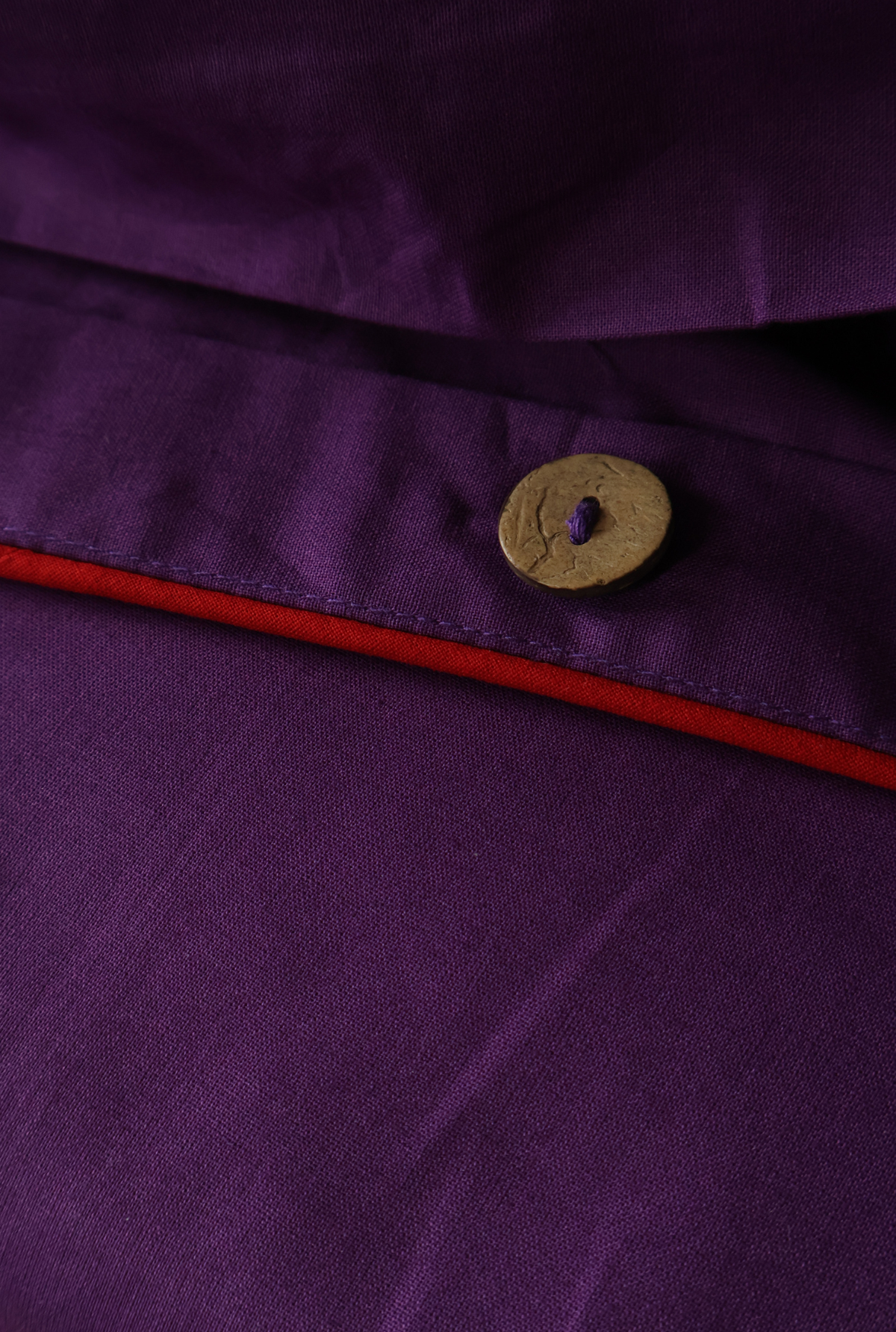 Close-up of a purple garment fabric with a small round gold button and a thin red trim line.