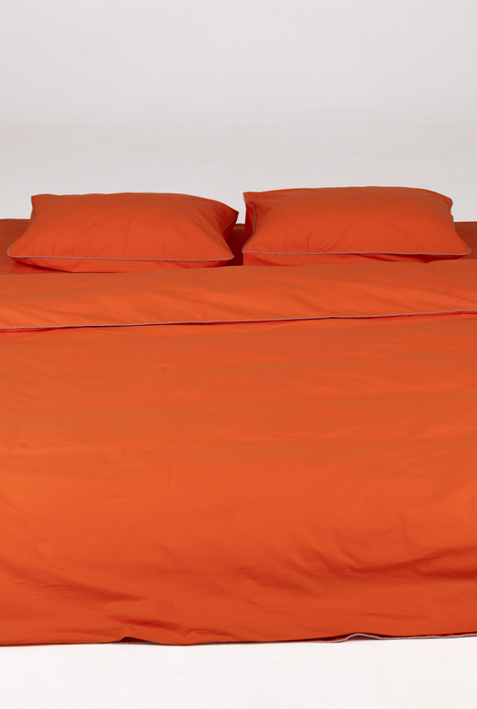 Bright orange bedding set including a duvet cover and two matching pillowcases, neatly arranged on a bed against a plain white background.