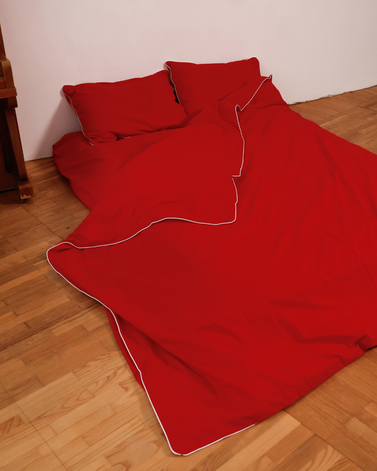 Red duvet and pillows on a wooden floor against a white wall