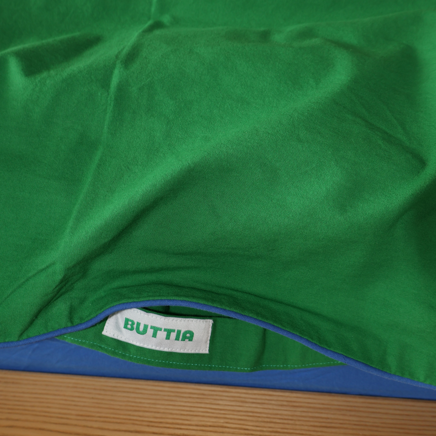 Close-up shot of the blue piping detail on a green cotton duvet cover by BUTTIA.