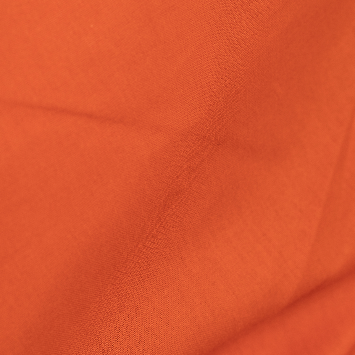 A close-up of textured orange sheet with soft folds and a fine woven pattern.