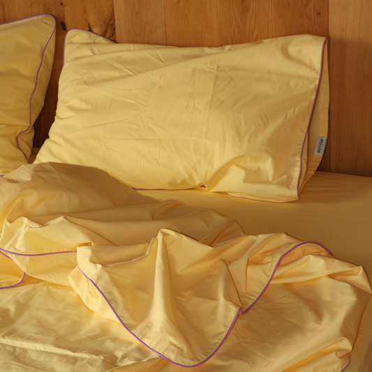 Natural yellow cotton bedding from BUTTIA with lavender piping details for a cozy bedroom interior.
