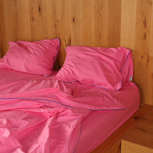 Pink bedding set on a bed against a wooden wall.