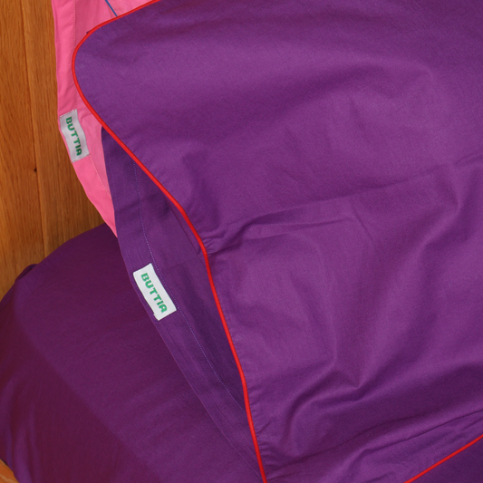 Close-up of BUTTIA purple pillowcase with elegant red piping detail and high quality stitching.