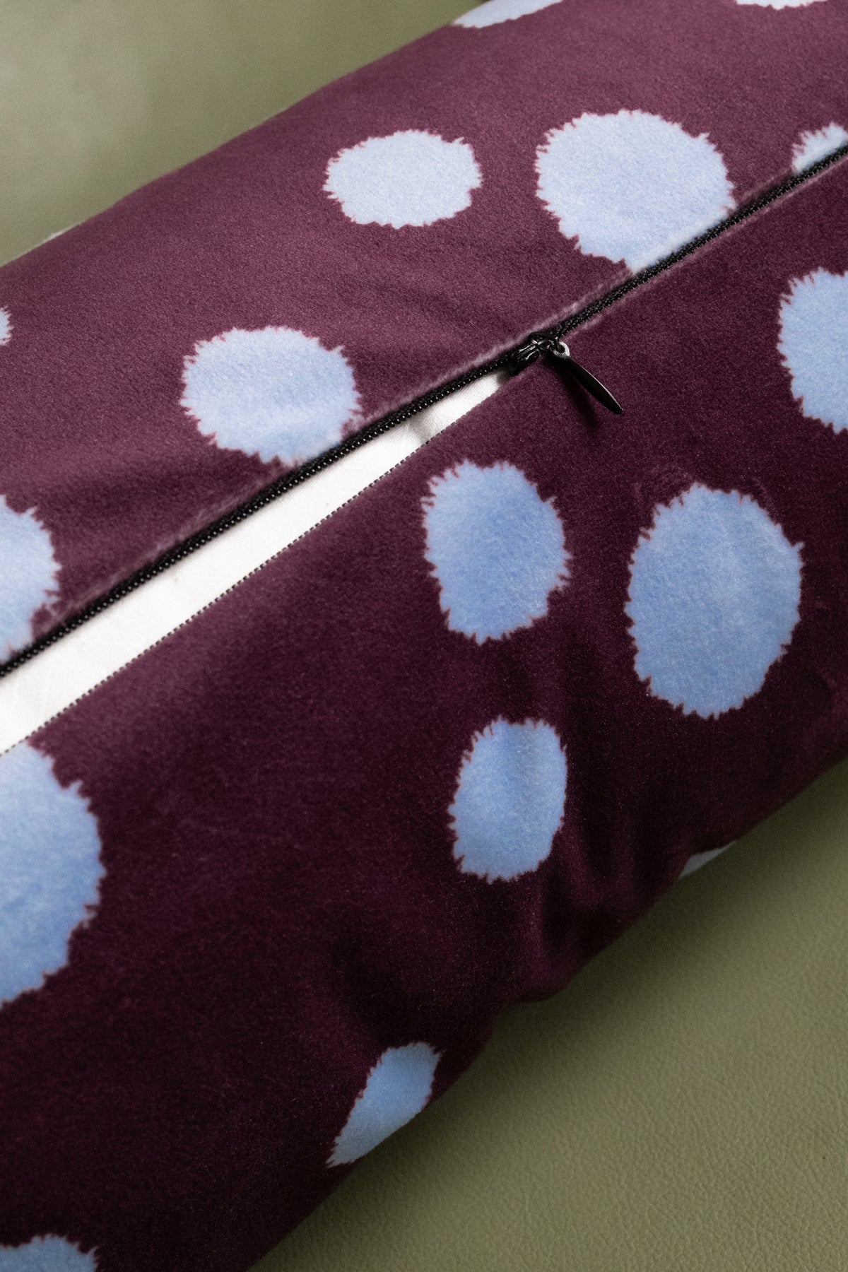 A close-up of a rectangular throw pillow with a deep purple and light blue polka dot pattern, featuring a black zipper closure.