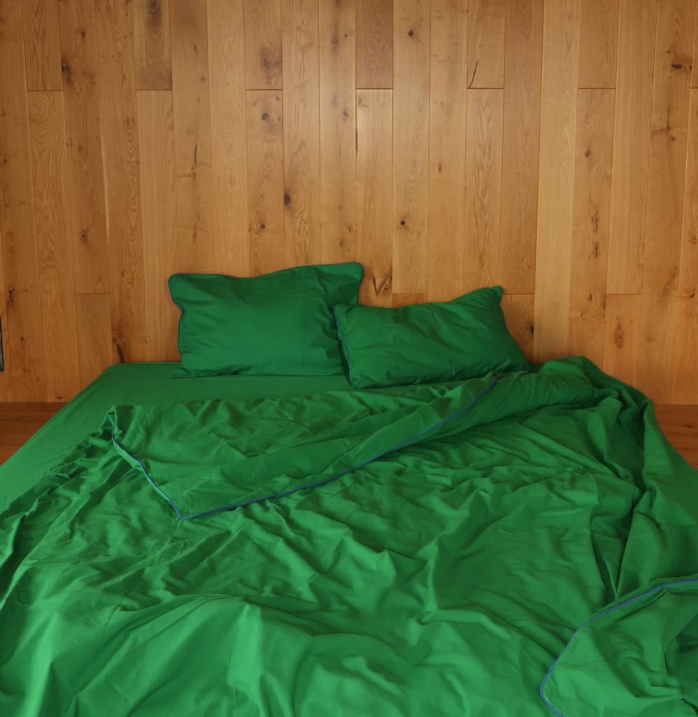 Complete green cotton bedding set by BUTTIA with a blue-piped duvet cover, bed sheet and two pillowcases.