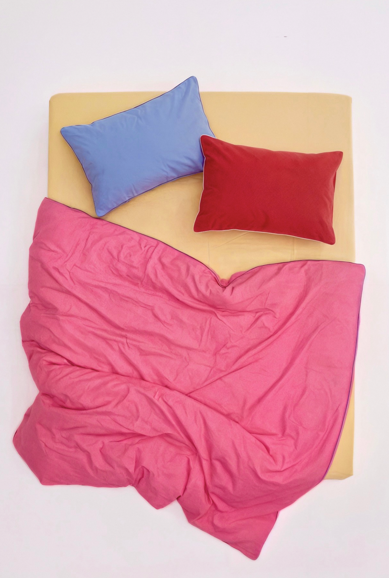 Pink blanket, blue pillow, and red pillow on a beige surface.