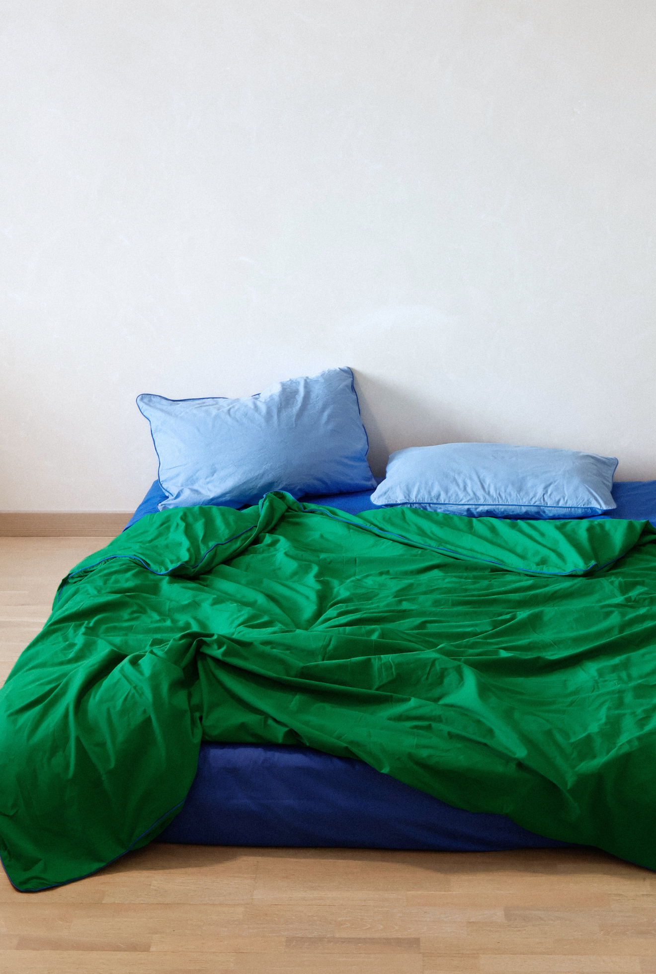 Bed with green bedding and blue pillows against a white wall.