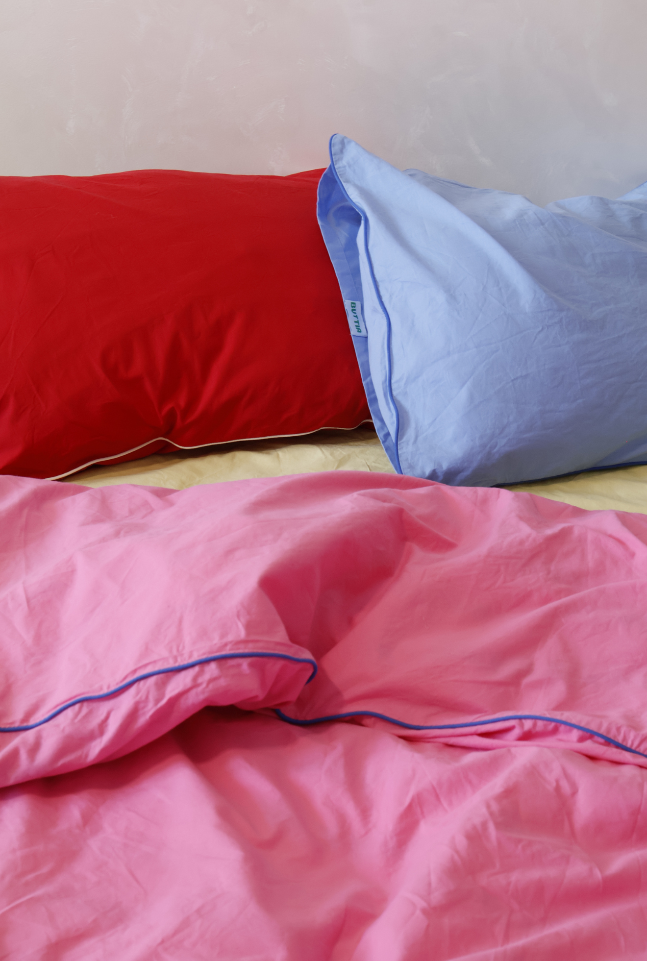 Red, blue, and pink bedding set on a bed with a light-colored wall in the background.