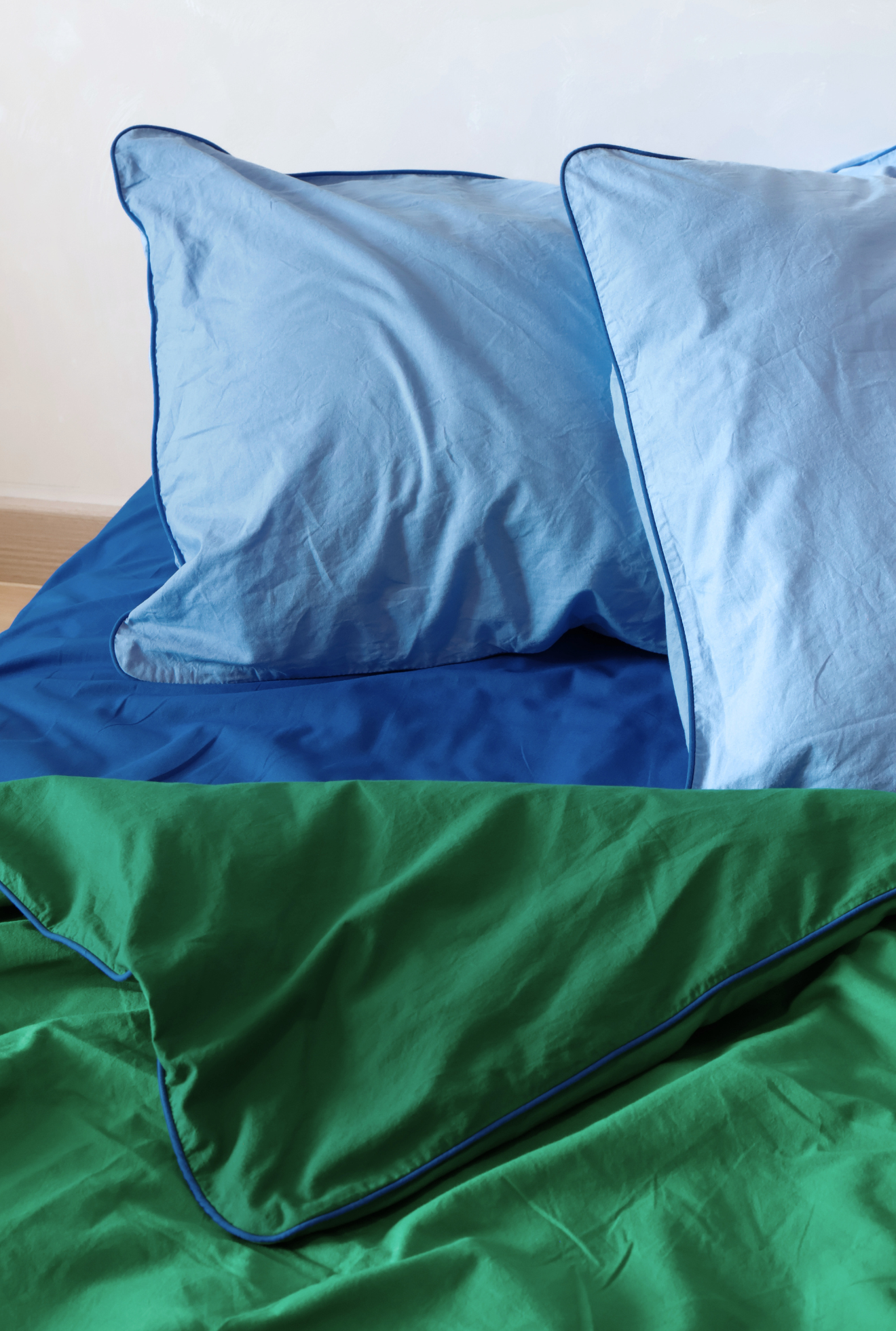 Two blue pillows on a bed with a white background, followed by a green comforter with a blue trim.