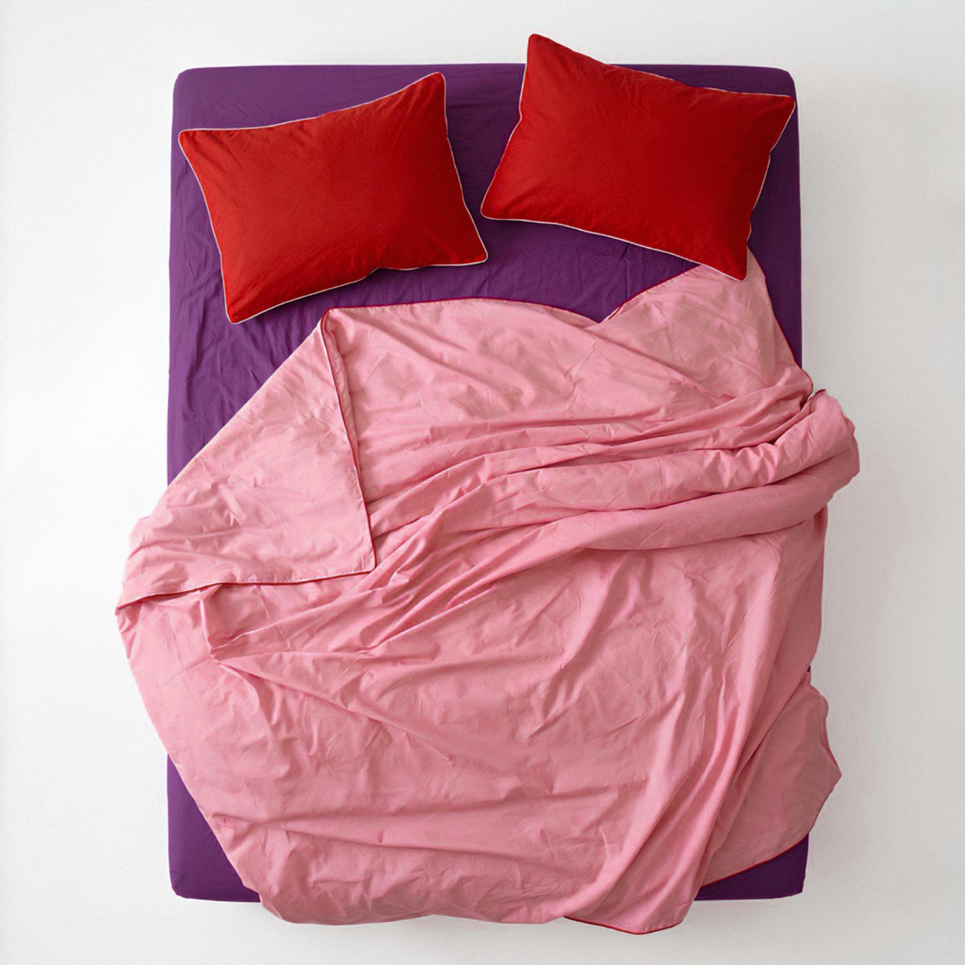 Pink comforter and red pillows on a purple bed frame against a white background