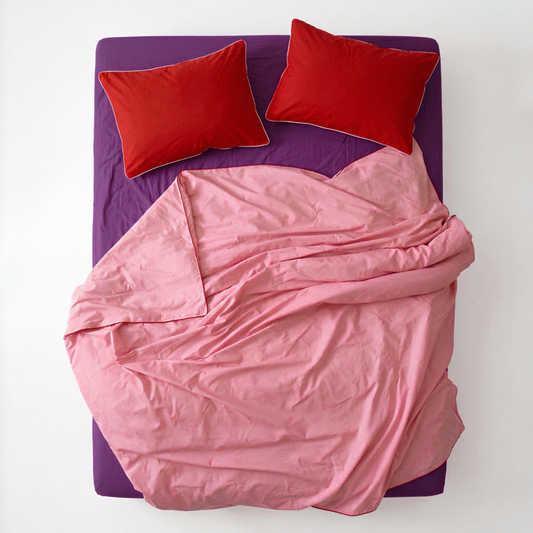 Pink comforter and red pillows on a purple bed frame against a white background