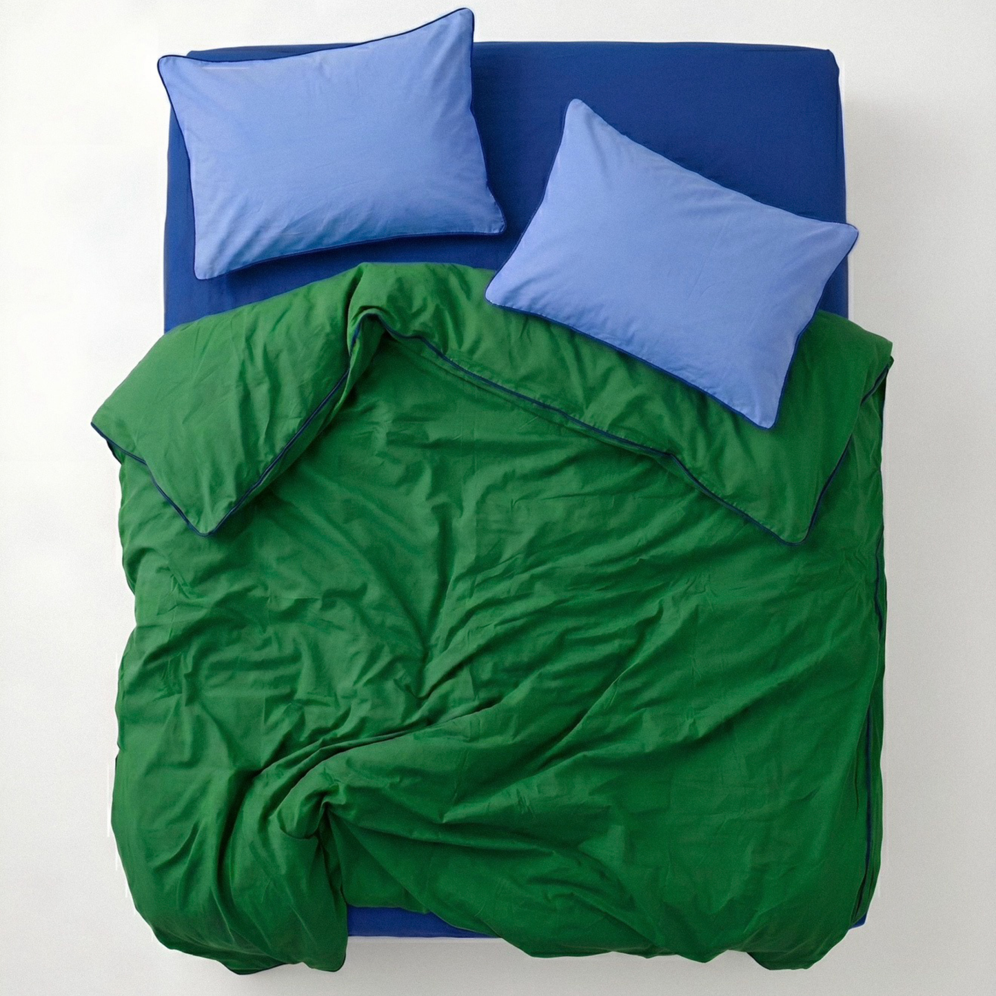 Green comforter and blue pillows on a bed with a white background