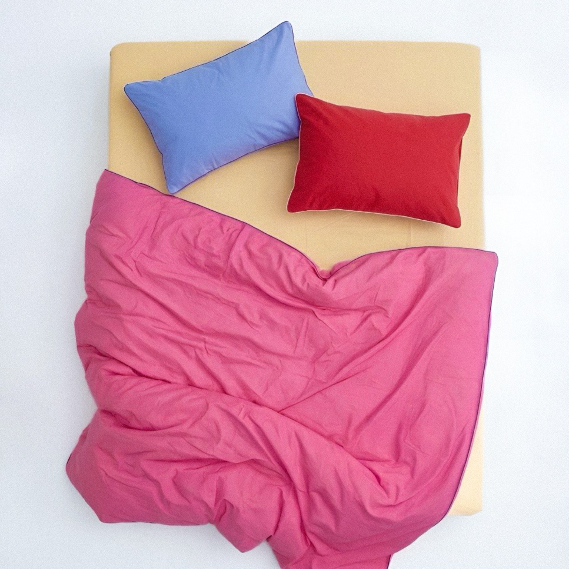 Pink comforter with blue and red pillows on a white background