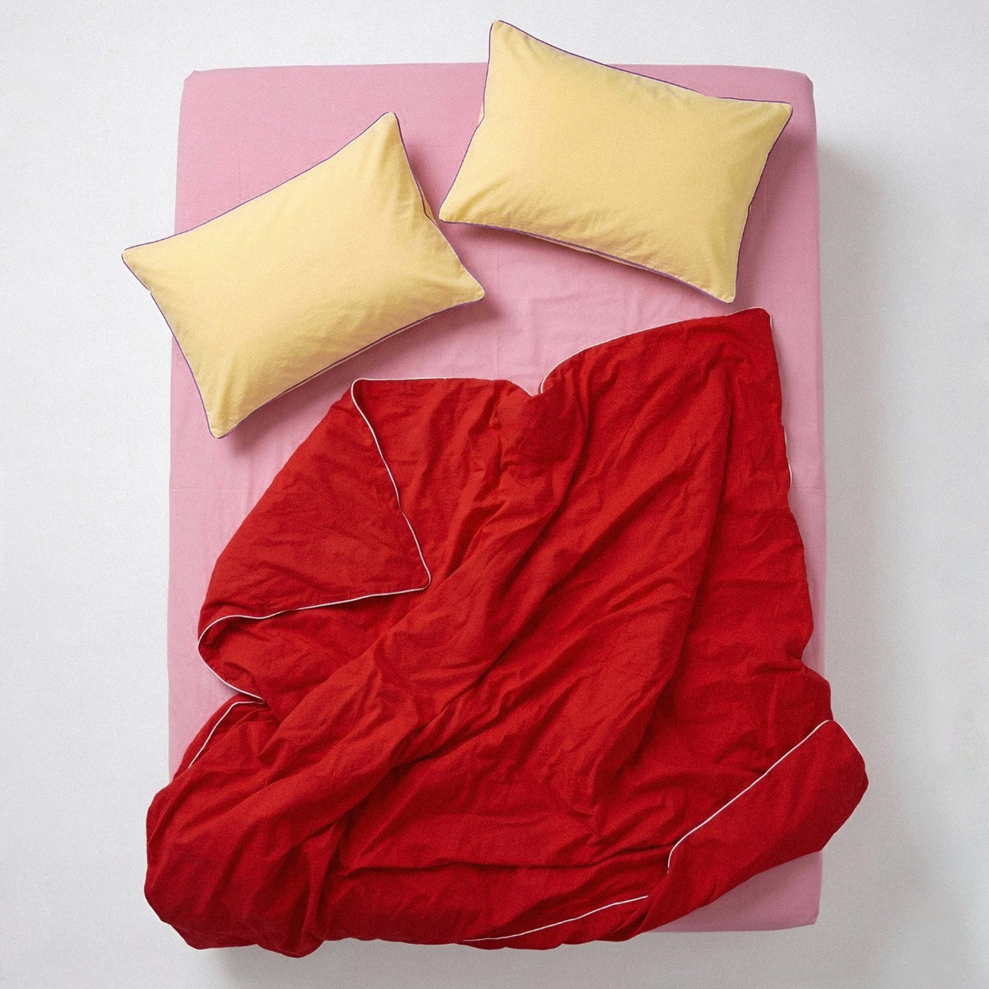 Red comforter on a pink bed with yellow pillows