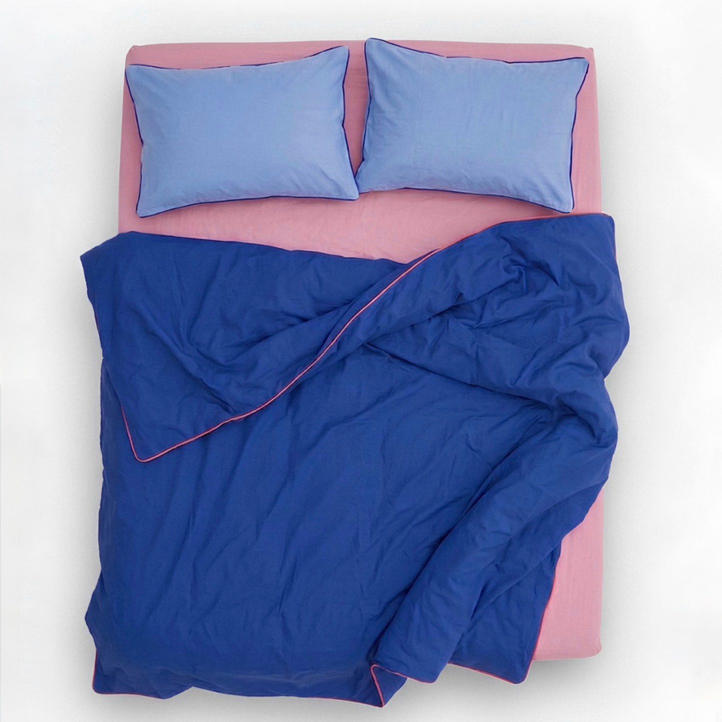 Blue and pink bedding set with light blue pillowcases, view from above. BORDERLINE Palette 06 by BUTTIA, handmade cotton bedding with orange accent piping.