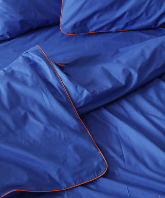 Close-up of blue BUTTIA bedding with orange piping