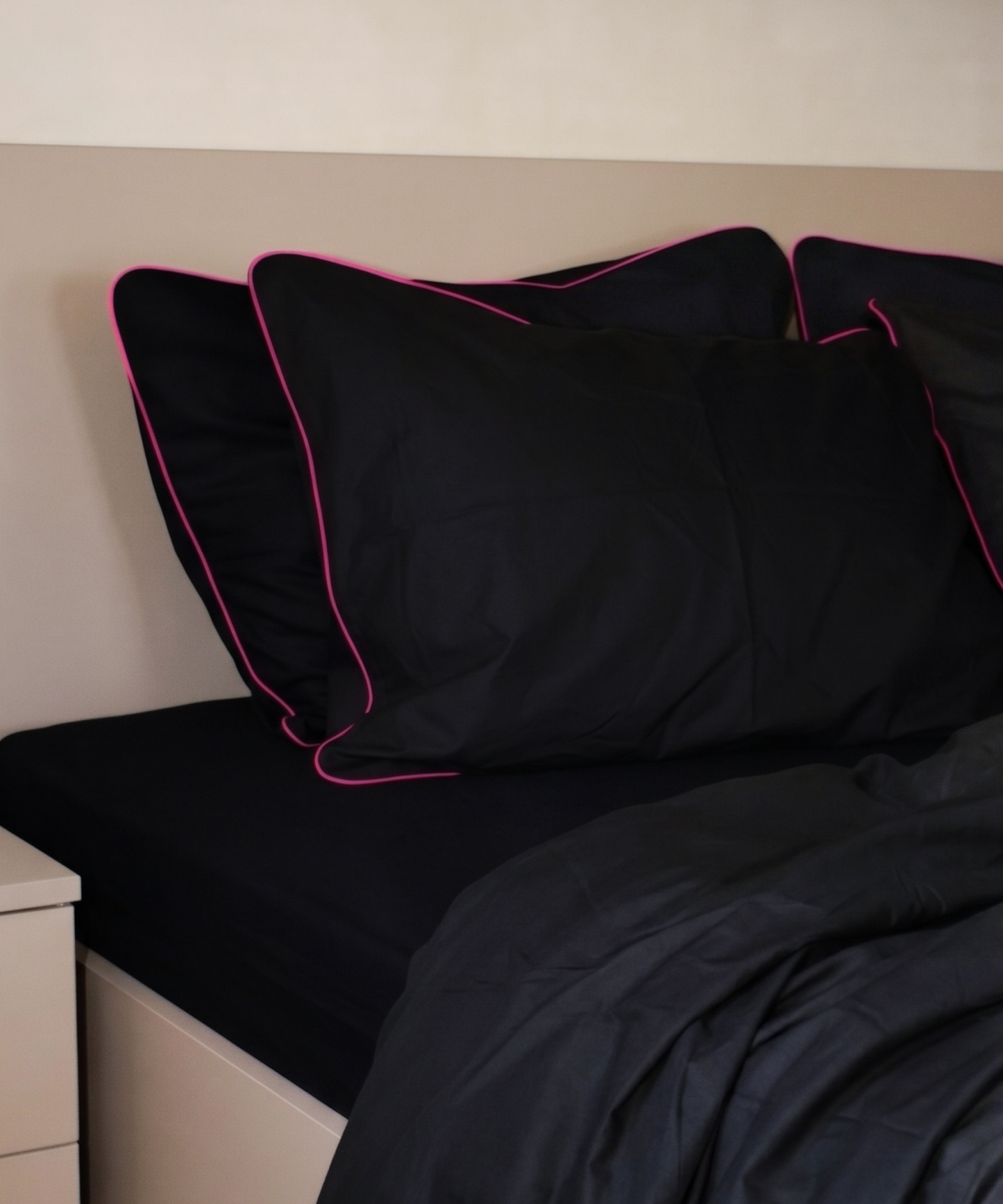 Black pillows with pink piping on a bed against a beige wall.