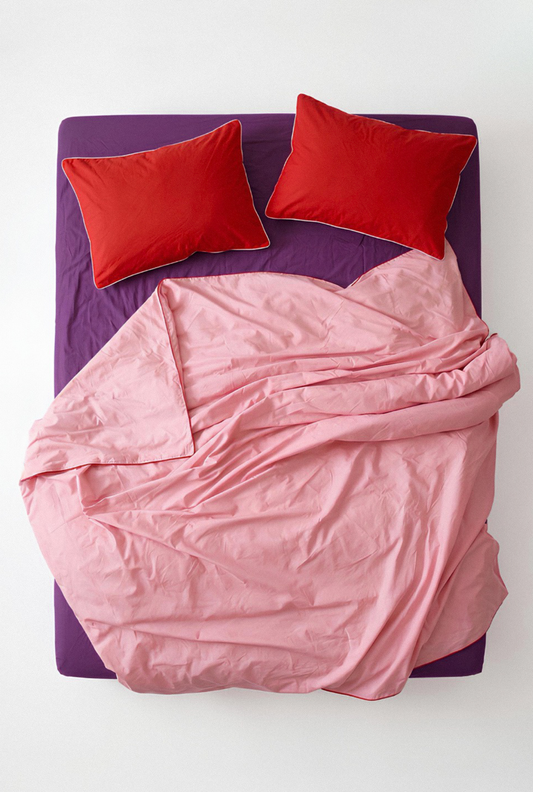 Pink comforter and red pillows on a purple bed frame against a white background