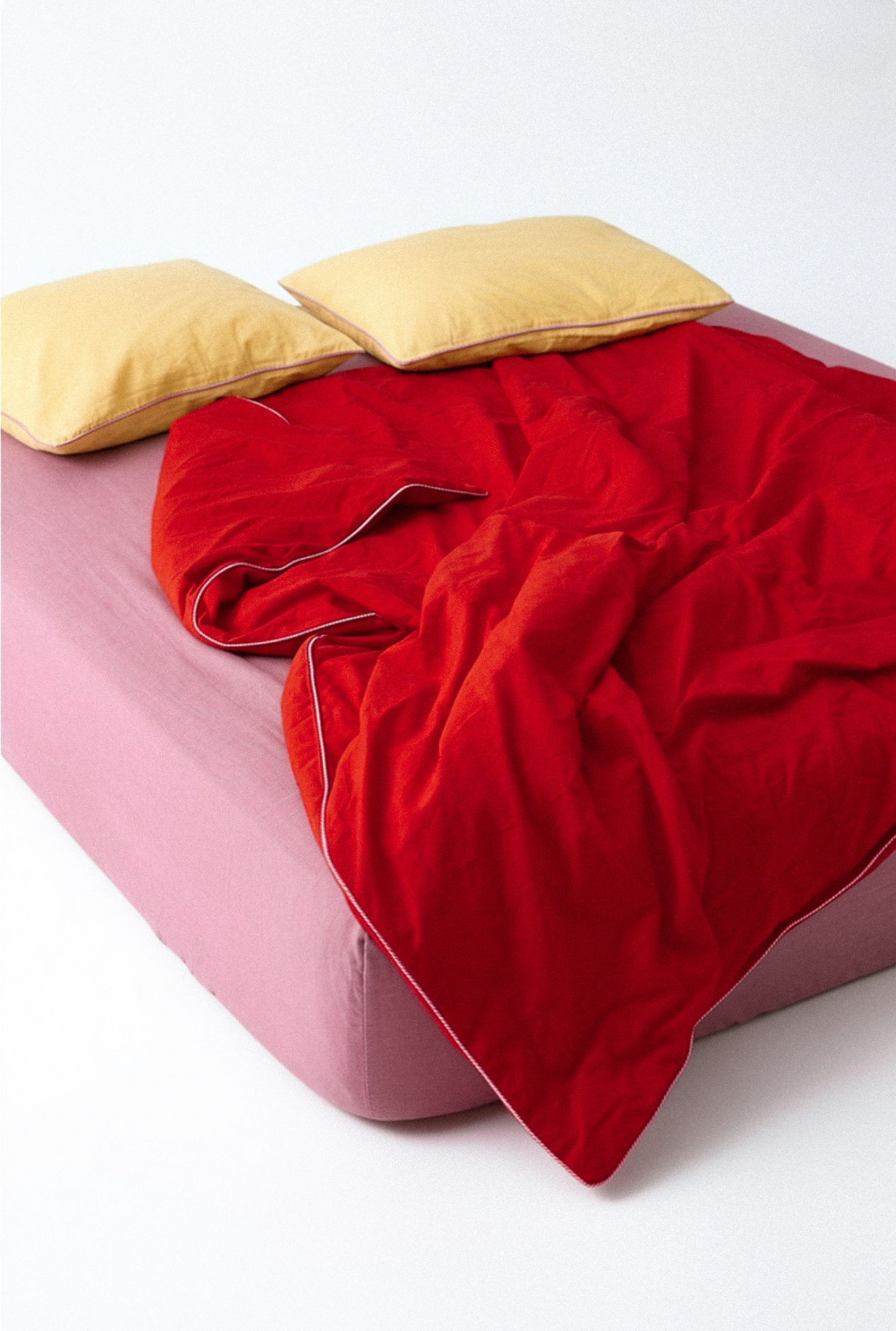 Red blanket on a pink bed with yellow pillows against a white background