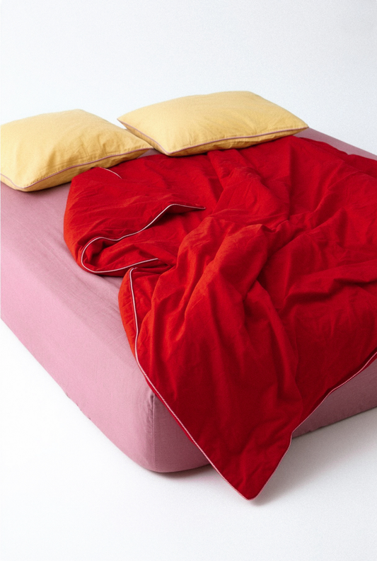 Red blanket on a pink bed with yellow pillows against a white background