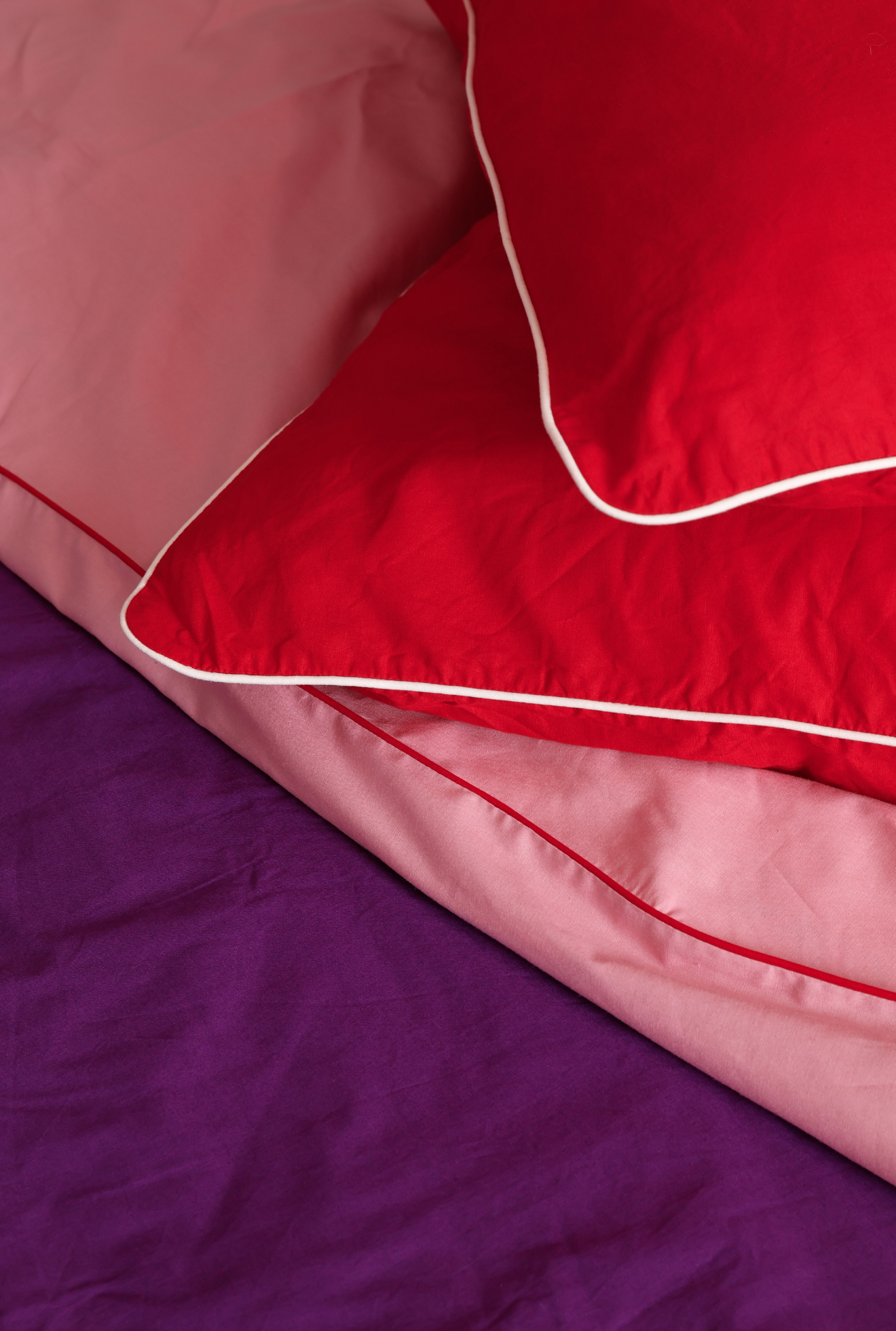 Close-up of red and pink bedding with white piping on a purple fabric background