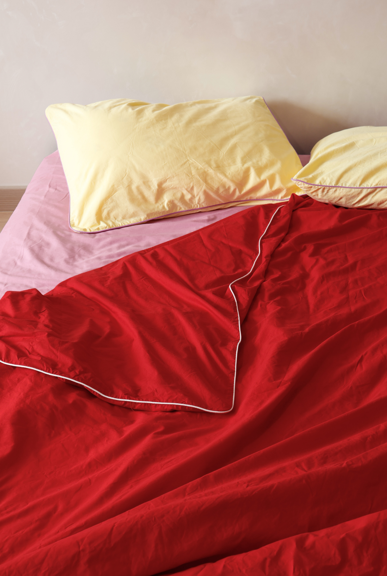 Red comforter with yellow pillows on a bed against a plain wall.