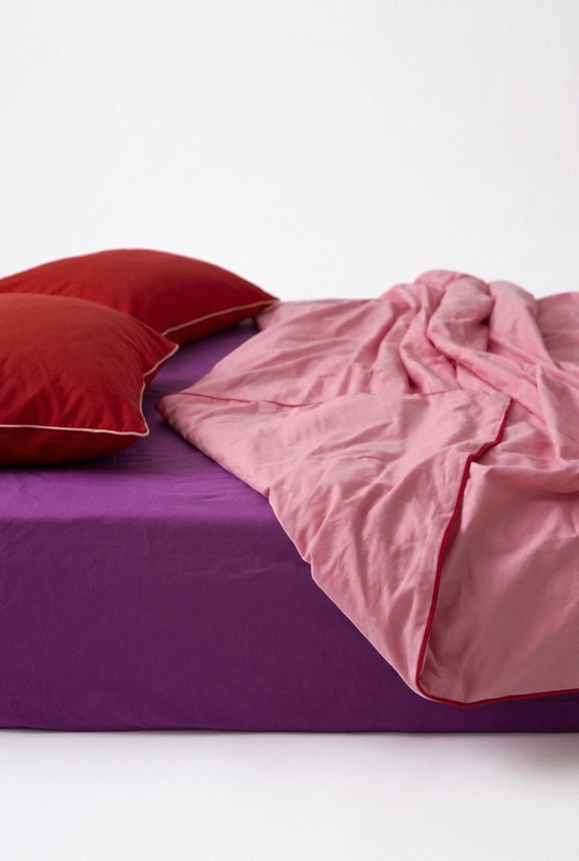 Bed with pink comforter and red pillows on a white background