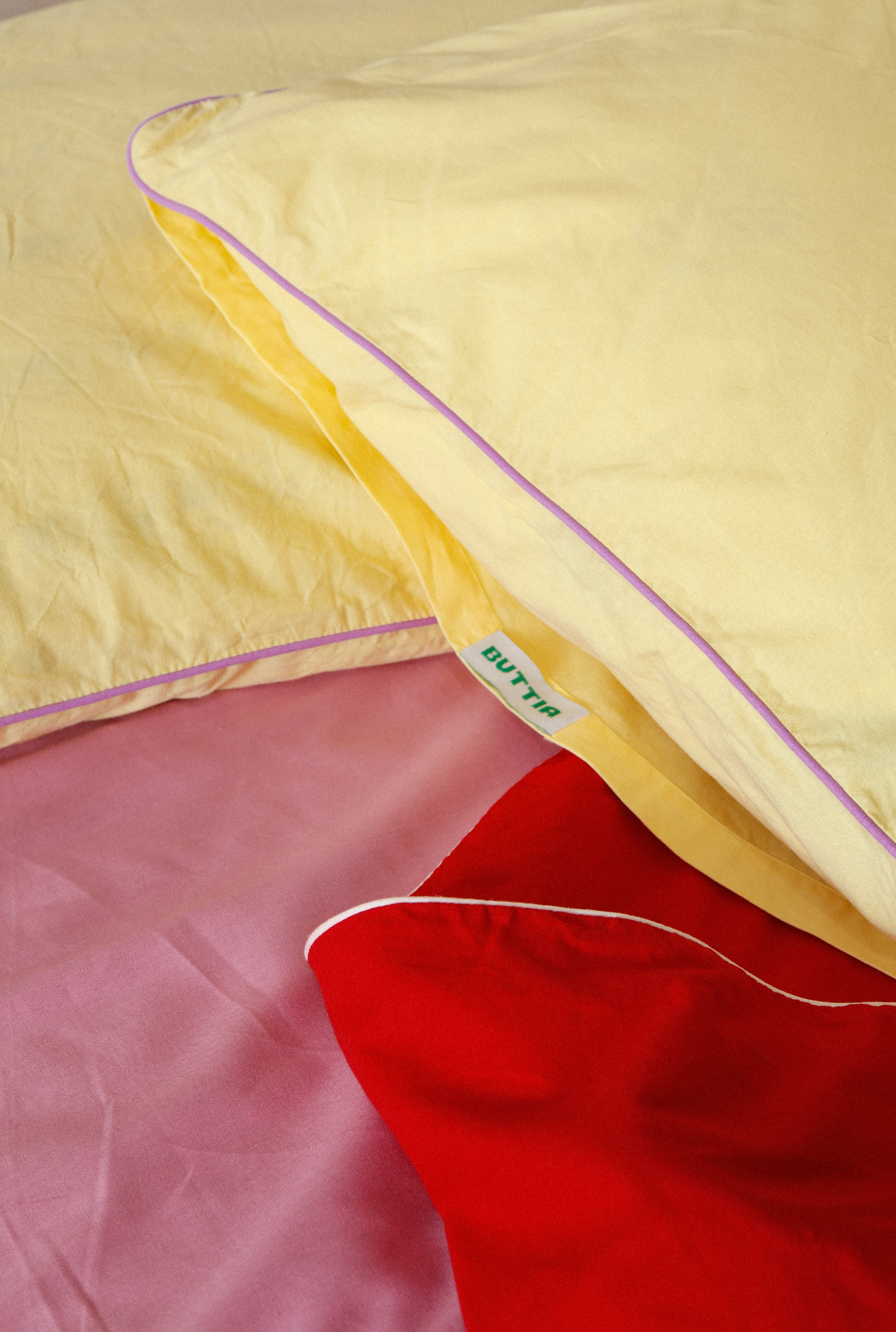 Close-up of a yellow pillow with a red blanket underneath on a pink surface.
