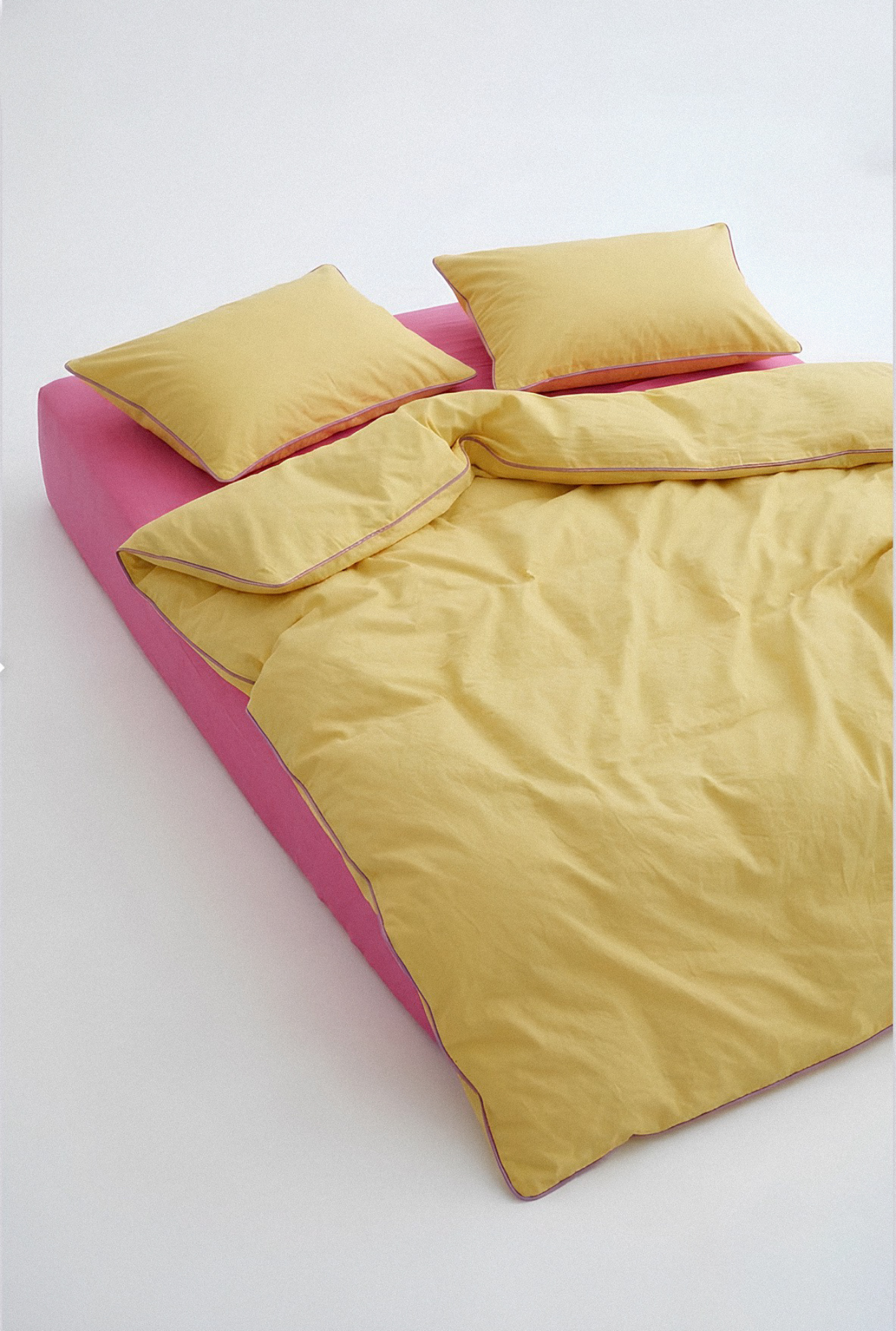 Yellow comforter and pillows on a pink bed frame against a white background