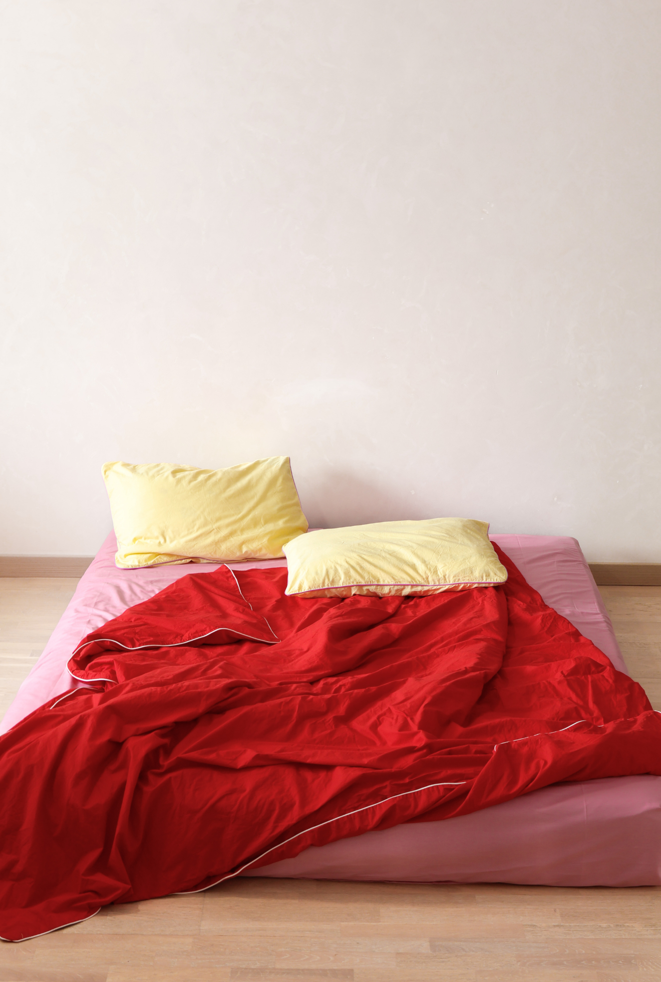 Bed with red blanket and yellow pillows against a white wall