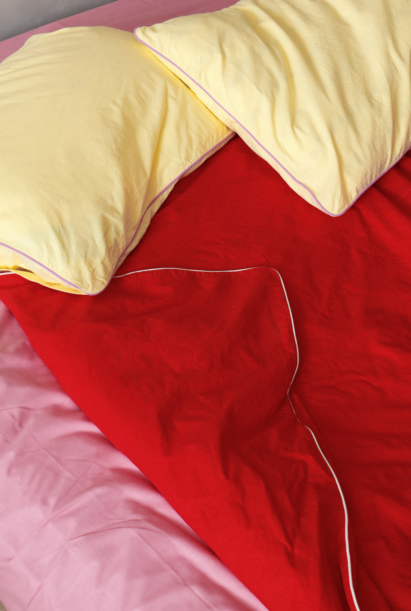 Close-up of a red blanket with white trim and yellow pillows on a bed.