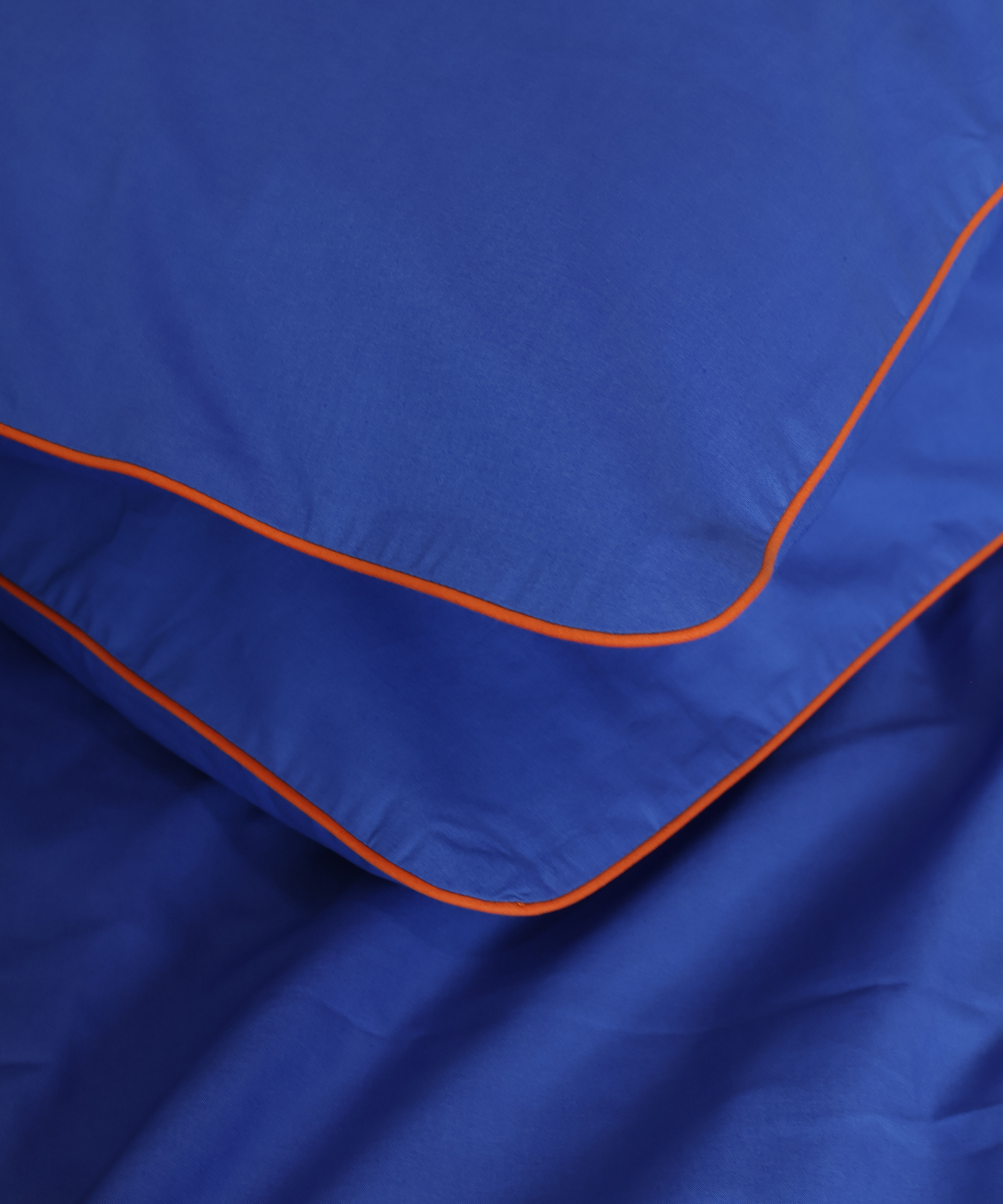 Bright blue cotton pillows with contrast orange piping by BUTTIA.