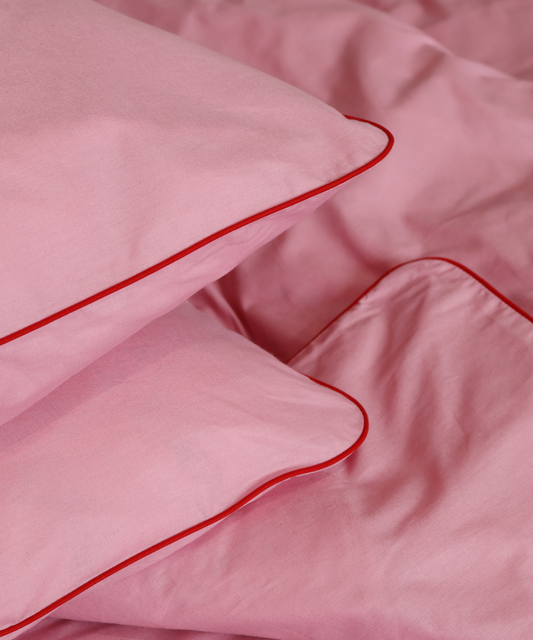 Pink bedding set with red piping on a soft pink background