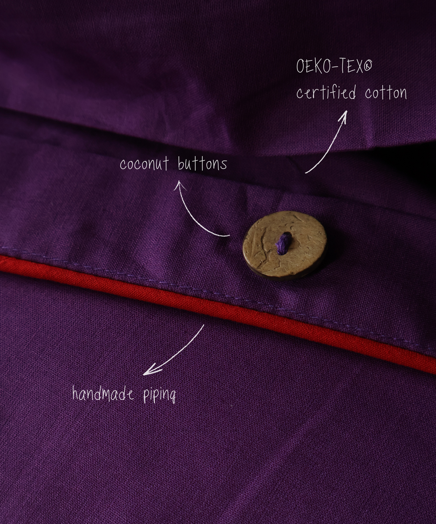 Close-up of a purple garment with a coconut button, OEKO-TEX certified cotton label, and red piping.