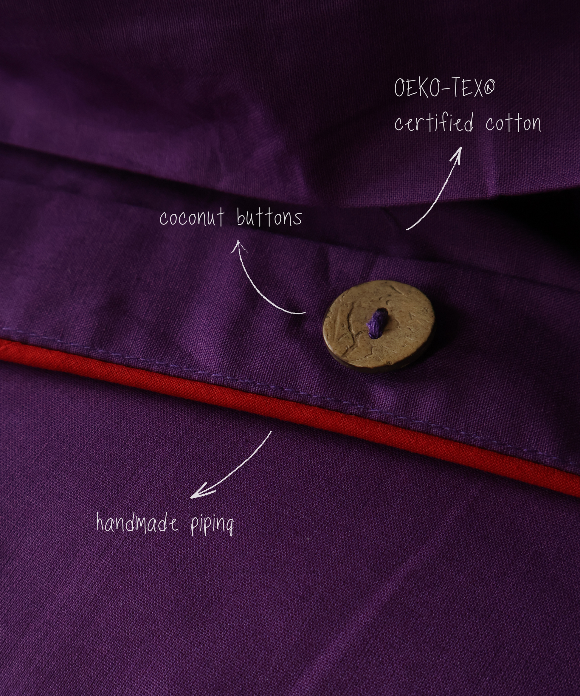 Close-up of a purple garment with a coconut button, OEKO-TEX certified cotton label, and red piping.