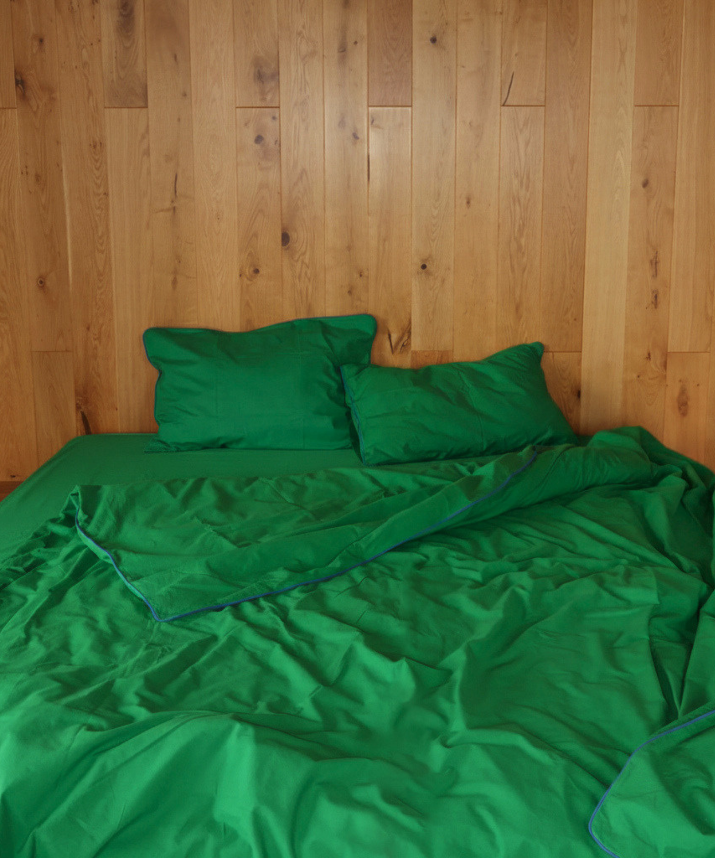 A bed made with bright green bedding, including a duvet cover and two matching pillows, set against a light brown wood-paneled wall.