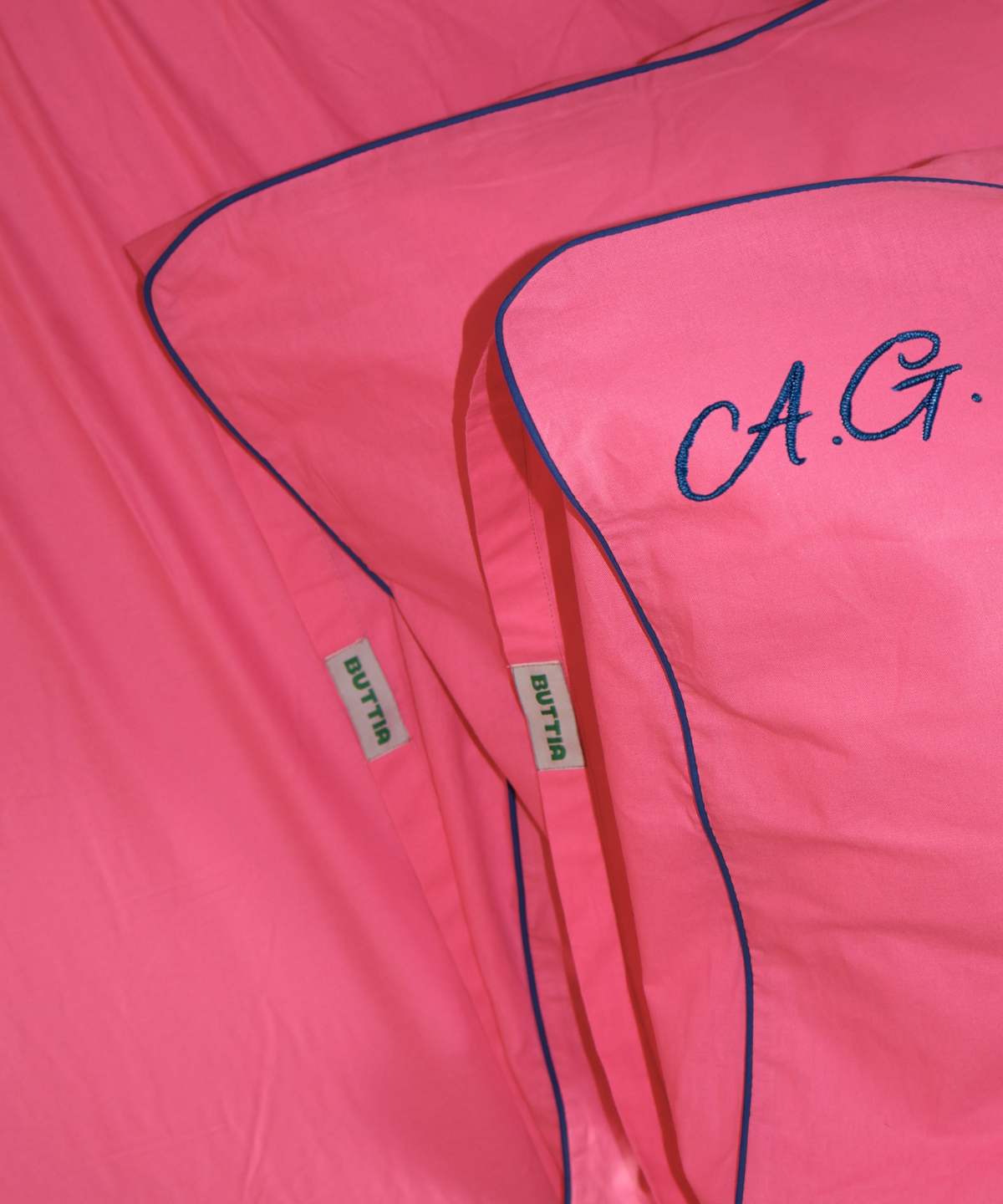 Close-up of a bright pink garment or fabric piece with blue piping, a red drawstring, and embroidered 'C.A.