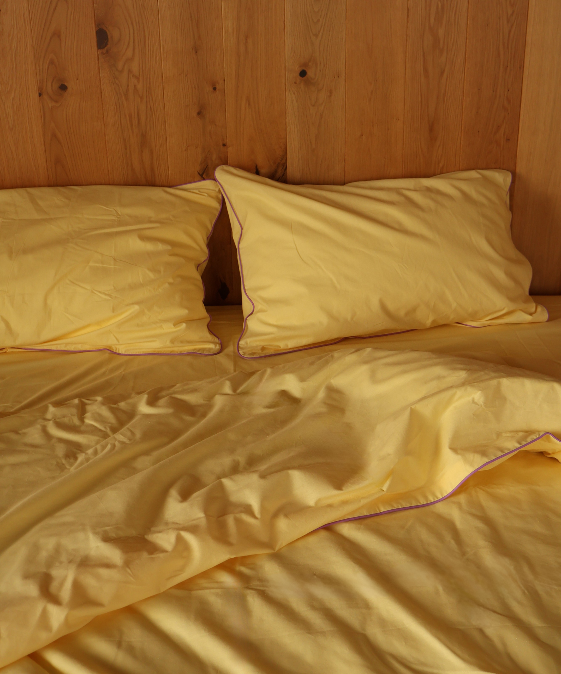 Yellow bedding set with two pillows and a rumpled duvet cover, styled on a bed against a wooden headboard.