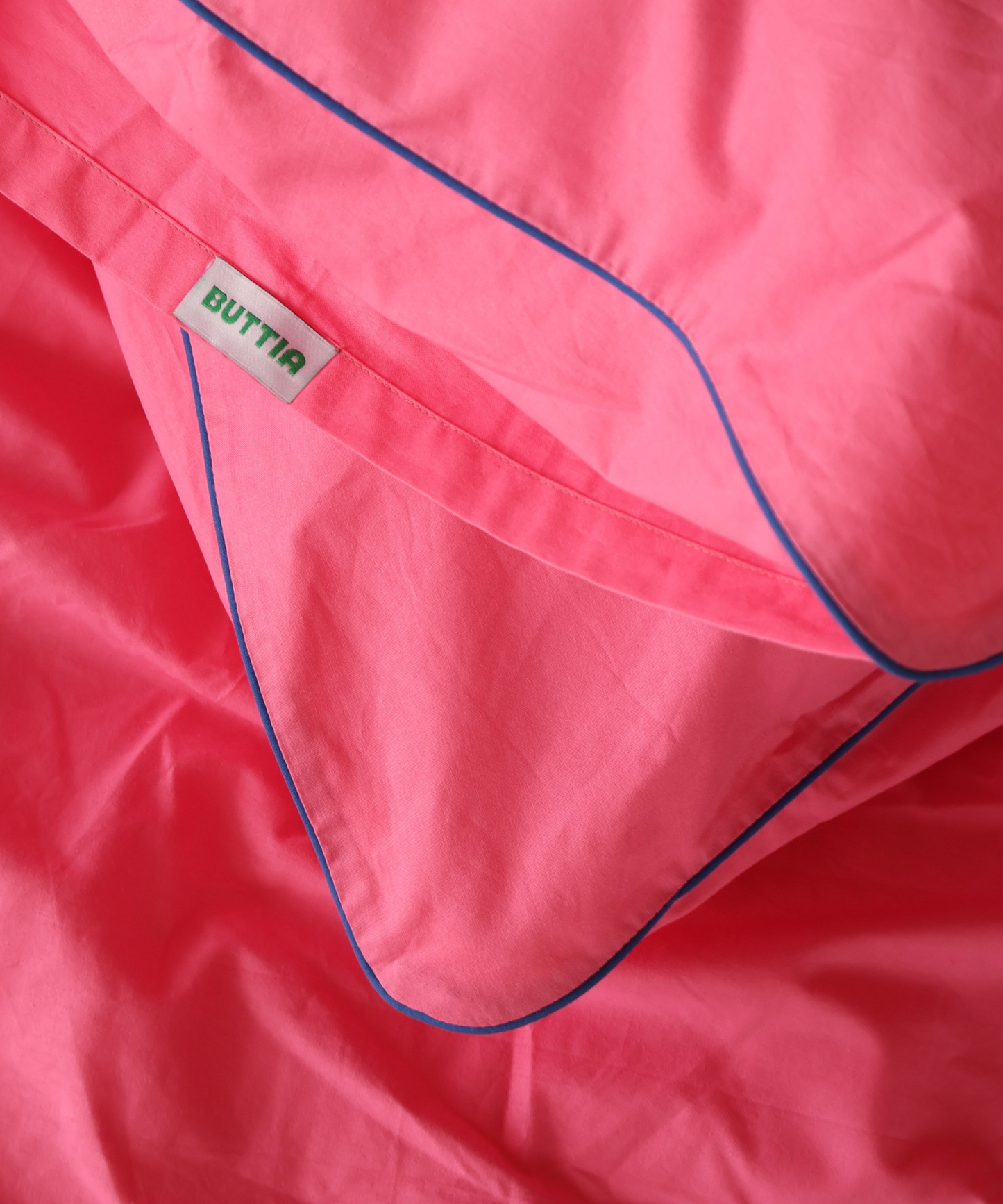 Close-up of a bright pink garment or fabric with blue piping and a small white brand tag reading BUTTIA.