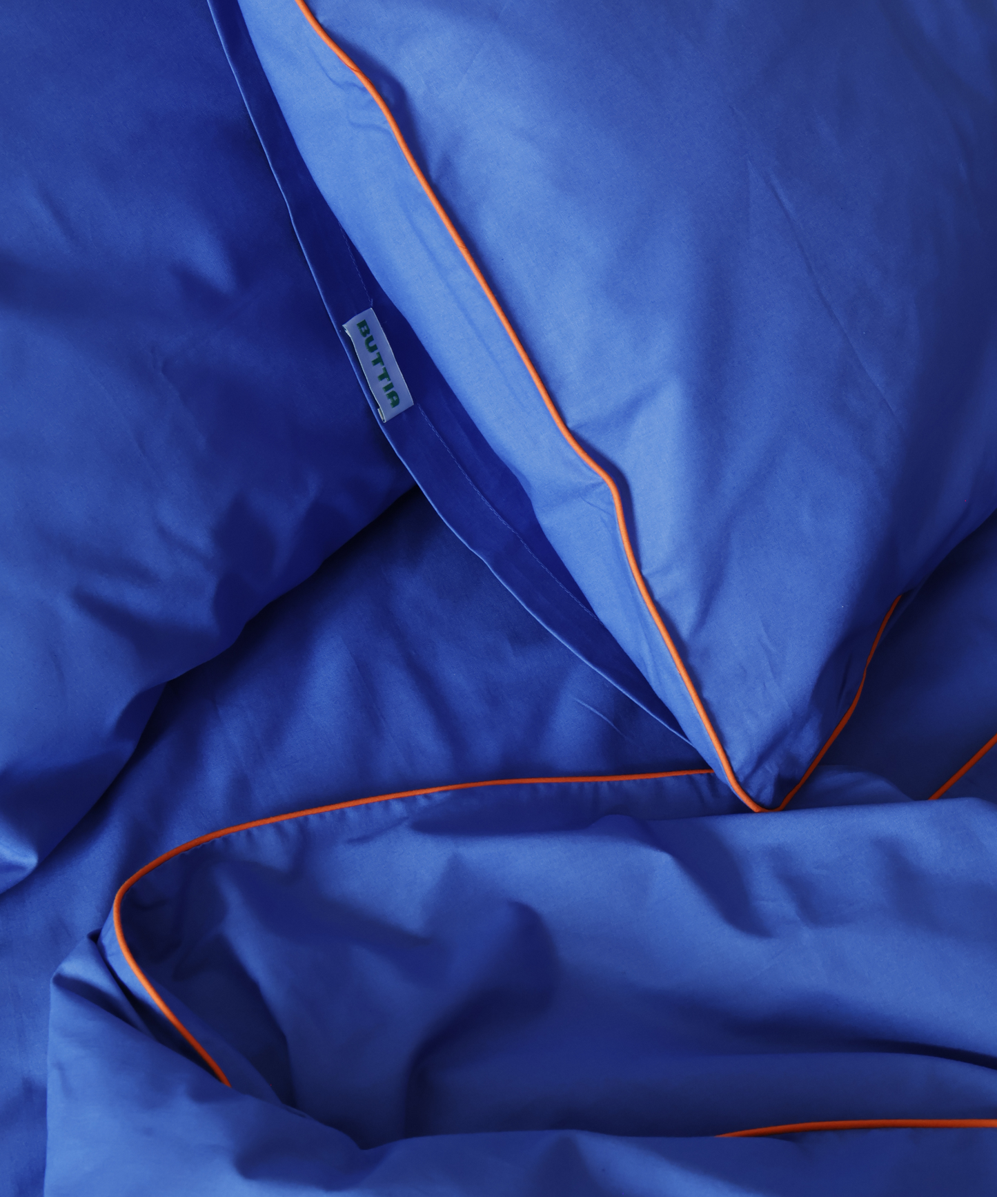 Close-up of blue fabric with orange piping and a brand label.